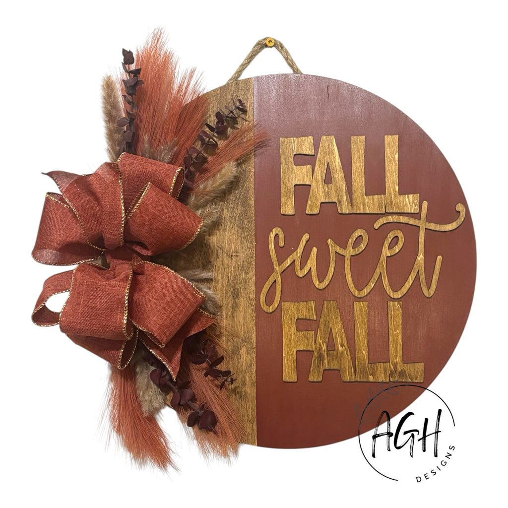AGH Designs circular wooden fall wall sign with Fall Sweet Fall text, burlap bow, and dried pampas grass foliage.